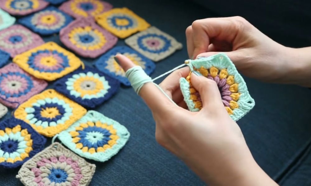 Hands crocheting a colorful granny square with a hook and yarn.