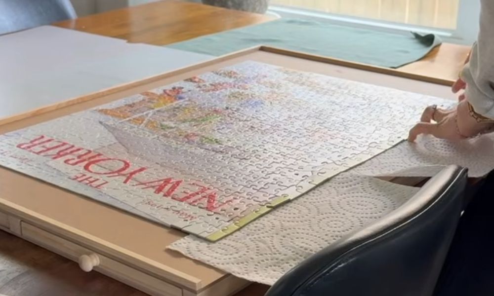 Large completed jigsaw puzzle being carefully positioned inside a wooden frame