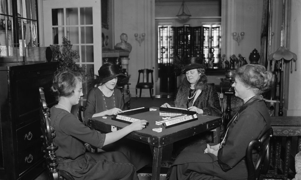 Black-and-white historical photograph of four women playing mahjong around a table.
