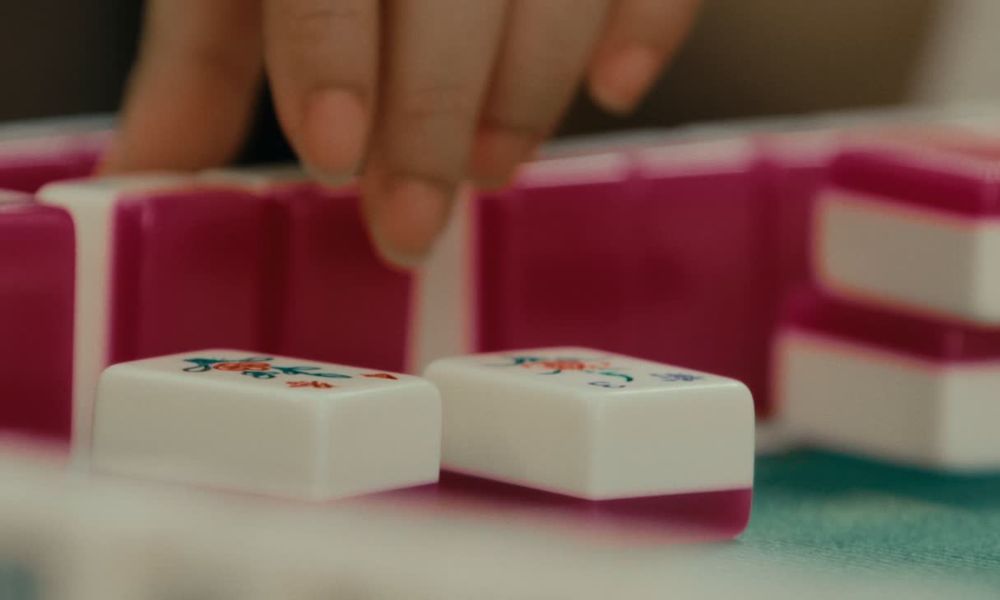 Close-up of a player arranging pink and white mahjong tiles during a game.