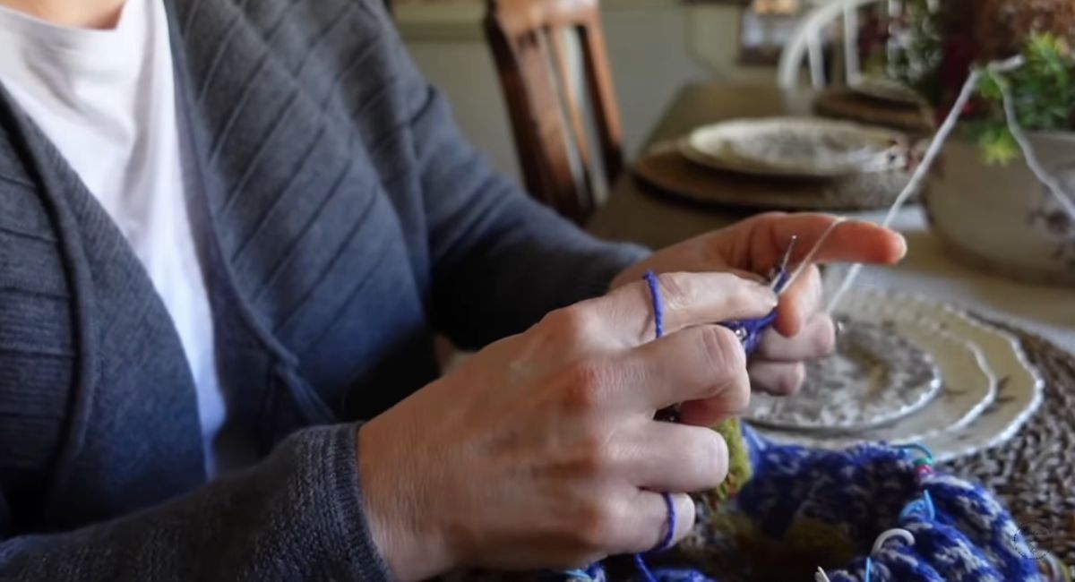 Person working on a knitting project with yarn and needles at a table.