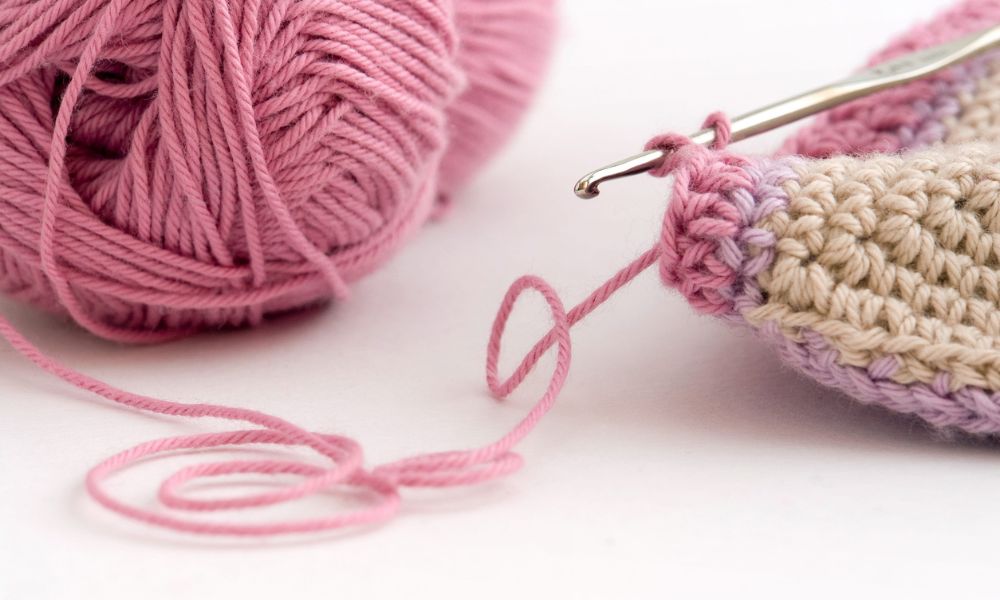 Close-up of pink yarn, a crochet hook, and handmade crochet stitches.